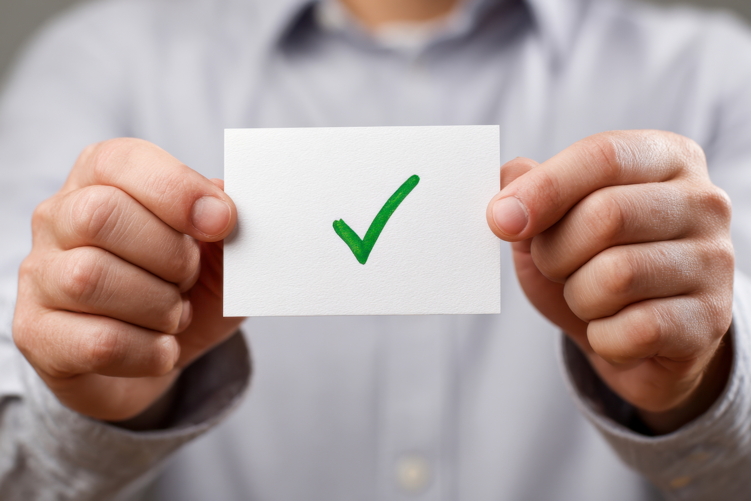 person-holding-white-card-with-green-check-mark-symbol-representing-approval-confirmation-blurred-background